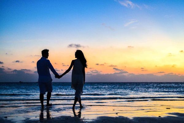 גבר ואישה מחזיקים ידיים והולכים על המים בחוף לאור שקיעה.